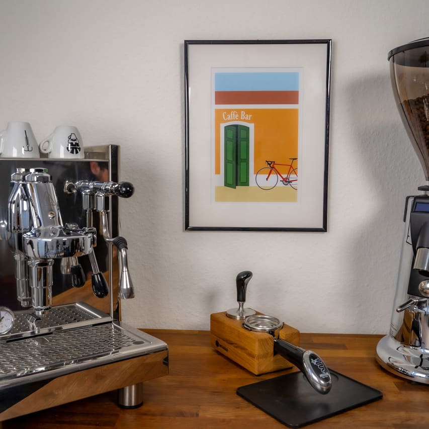 Das Poster "Caffè Bar" hängt im Bilderrahmen an der Wand zwischen einer Kaffeemaschine und einer Kaffeemühle.