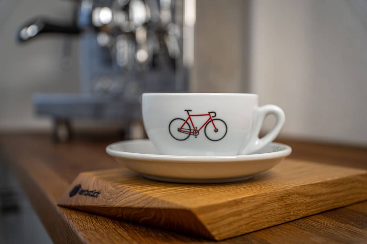 Eine weiße Cappuccino-Tasse mit einem roten Rennrad in seitlicher Darstellung.