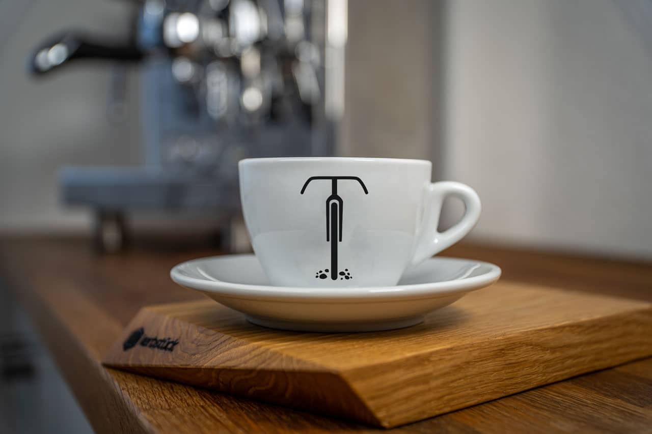 Eine weiße Cappuccino-Tasse bedruckt mit der schwarzen Silhouette eines Gravel-Rades