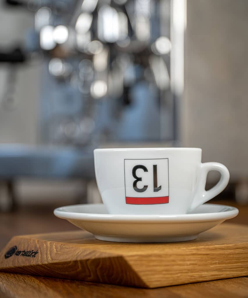 Eine weiße Cappuccino-Tasse bedruckt mit einer umgedrehten 13 als stilisierte Rückennummer.