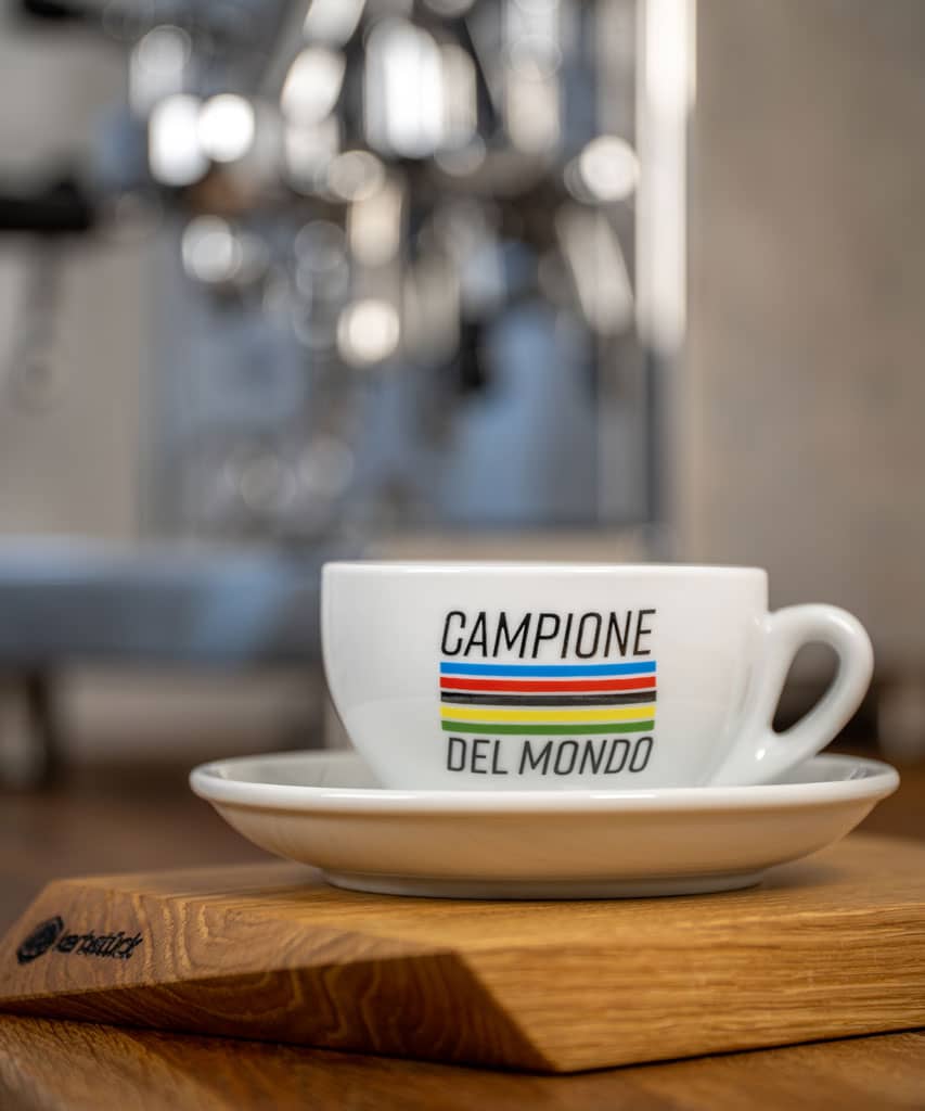 Eine weiße Cappuccino-Tasse mit fünf Streifen in Regenbogenfarben und dem Schriftzug Campione del Mondo