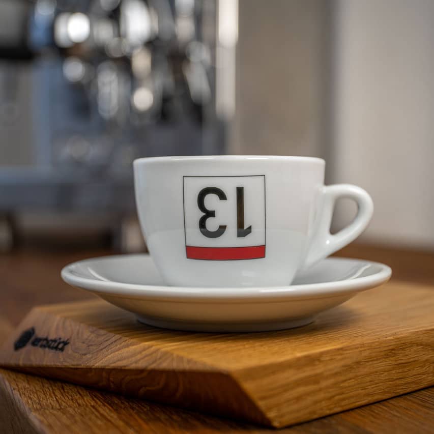 Eine weiße Cappuccino-Tasse bedruckt mit einer umgedrehten 13 als stilisierte Rückennummer.