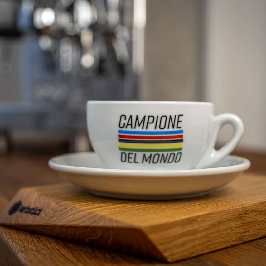 Eine weiße Cappuccino--Tasse mit fünf Streifen in Regenbogenfarben und dem Schriftzug Campione del Mondo