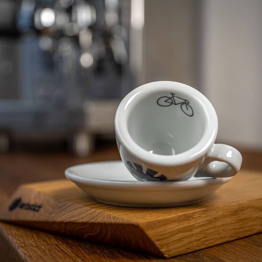 Eine Espresso-Tasse liegt auf der Seite, auf dem inneren Tassenrand ist ein Rennrad abgedruckt.