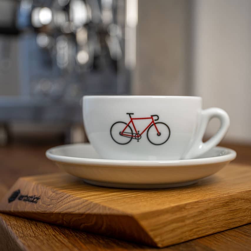 Eine weiße Cappuccino-Tasse mit einem roten Rennrad in seitlicher Darstellung.