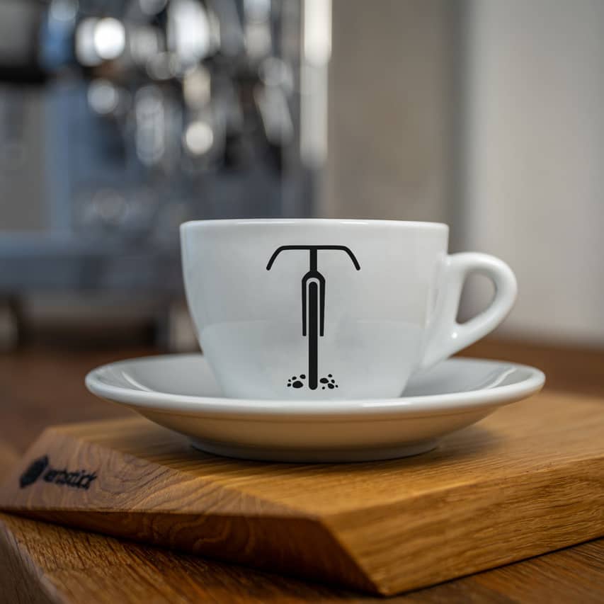 Eine weiße Cappuccino-Tasse bedruckt mit der schwarzen Silhouette eines Gravel-Rades