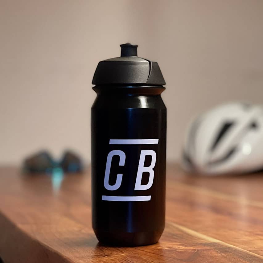 Eine schwarze Fahrrad-Trinkflasche mit dem Logo von CYCLEBEAN auf einem Tisch vor einem verschwommenen Hintergrund.
